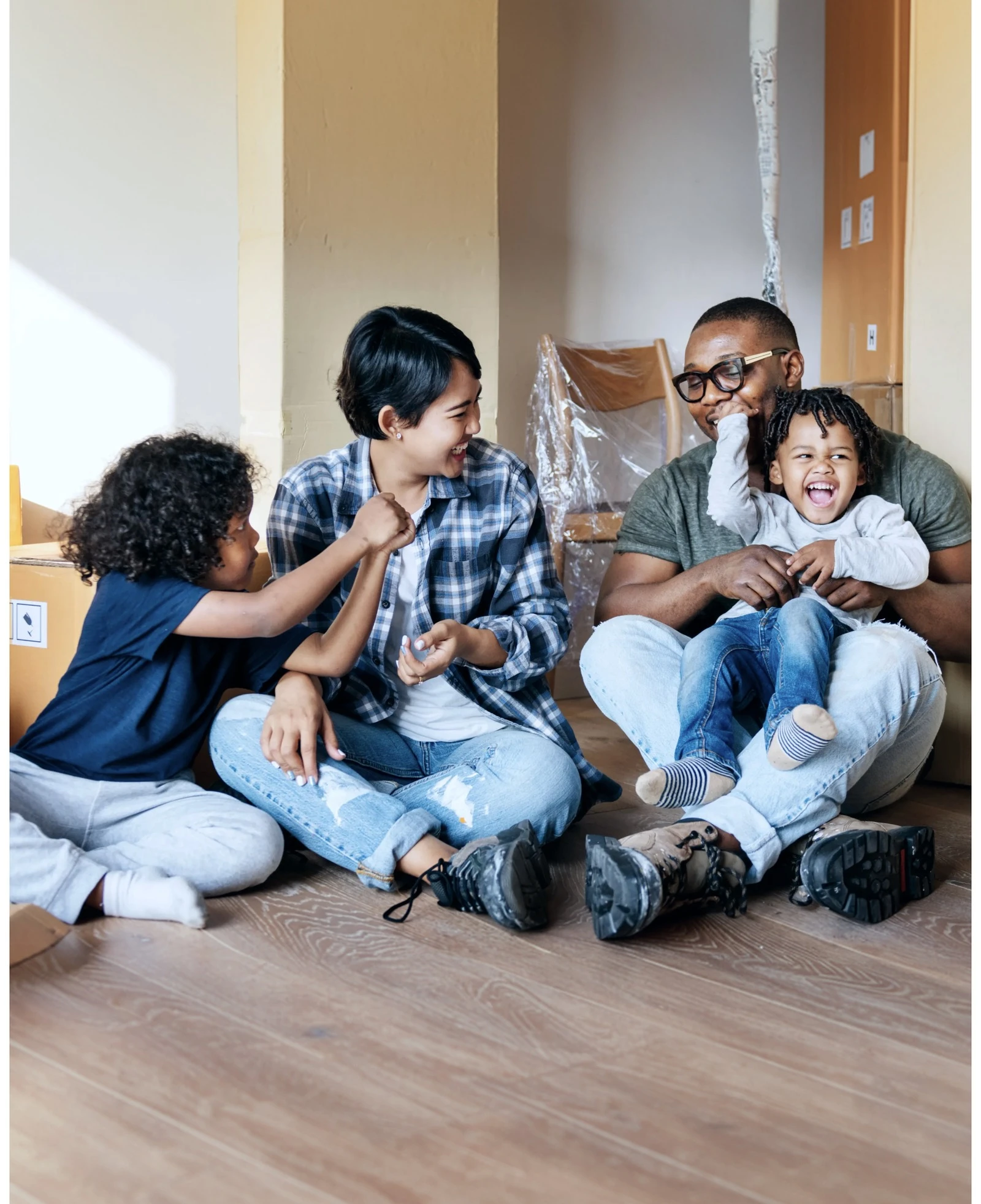 A laughing family with two young children sitting on the floor of their new home among moving boxes