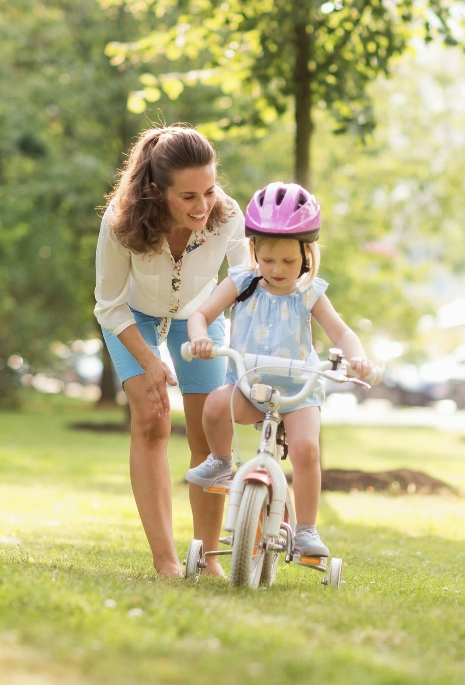 A smiling mother helping her young daughter ride a bike